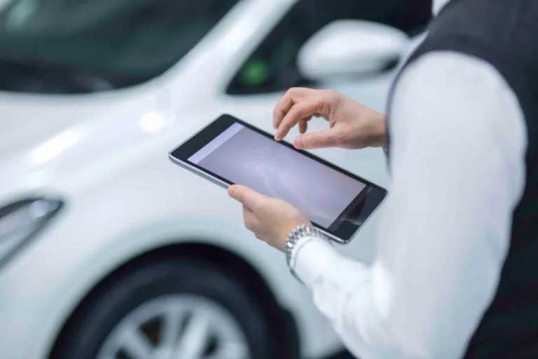 Person using a tablet beside a white car