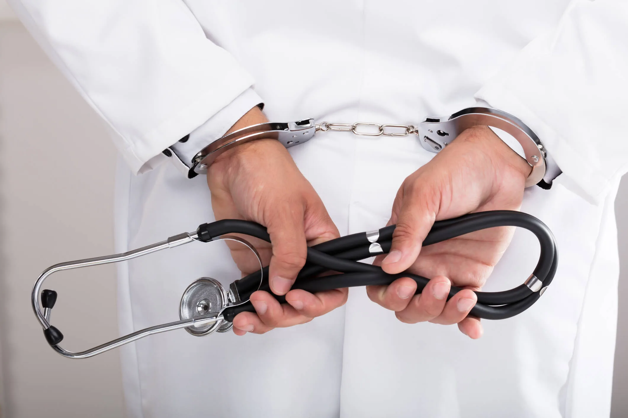 Doctor in handcuffs holding a stethoscope behind back
