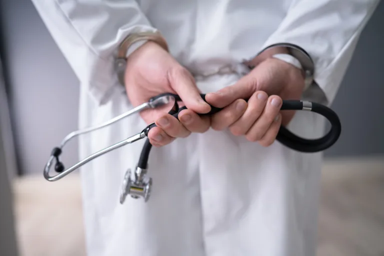 Doctor in white coat handcuffed, holding stethoscope — medical misconduct concept