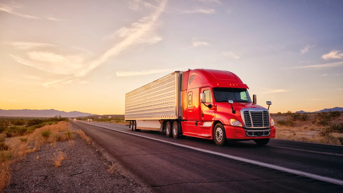 Red semi-truck hauling a trailer on a desert highway at sunset