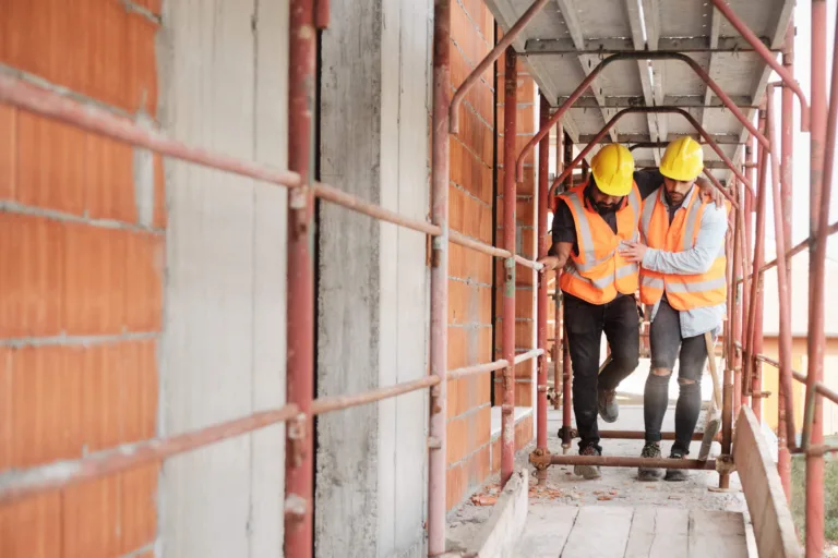 Construction worker helps injured coworker along scaffolding walkway