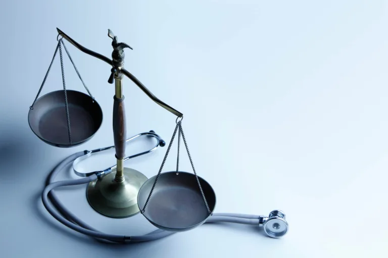 Scales of justice with stethoscope on a pale blue surface