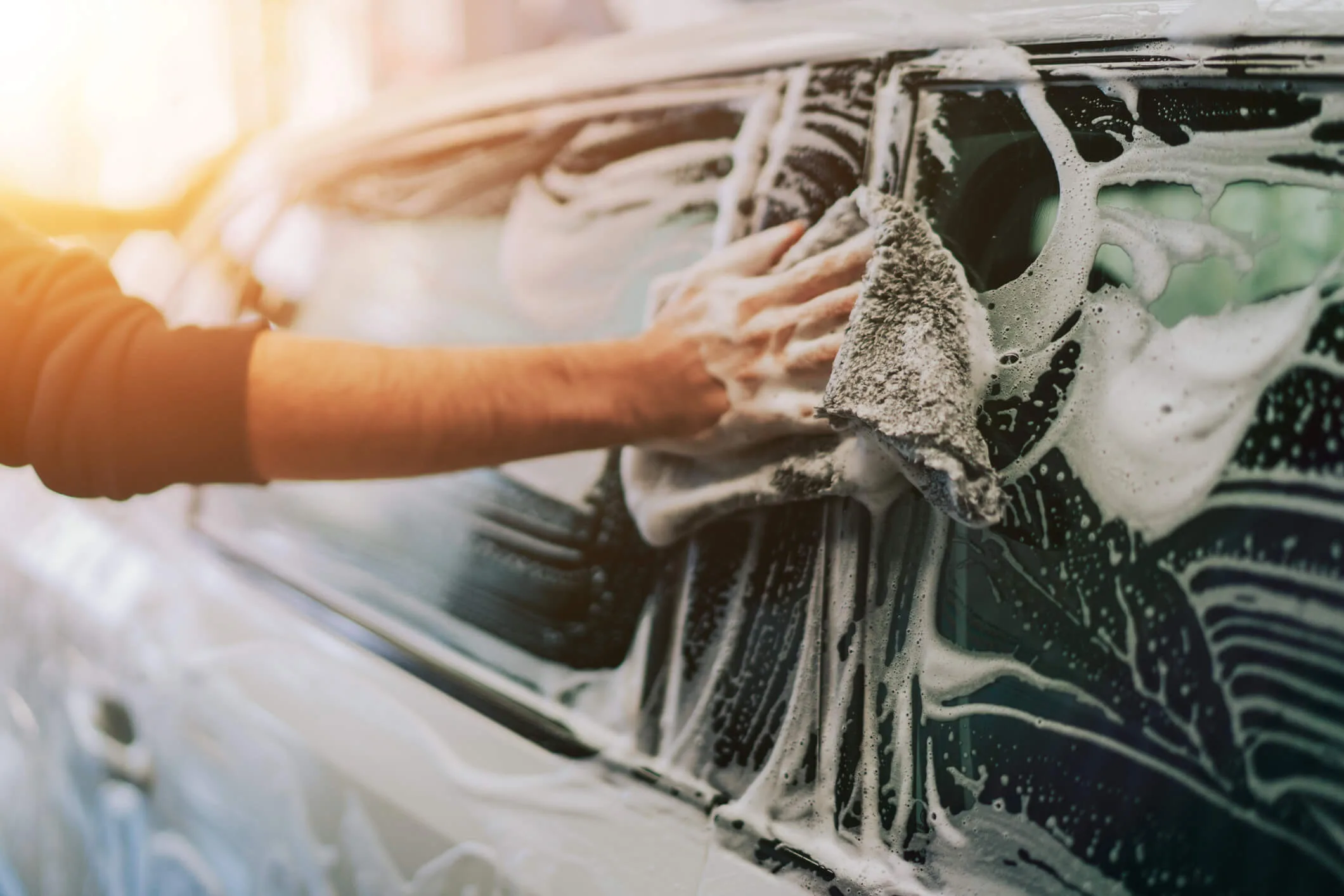 Close-up of hand washing a car window with soap suds