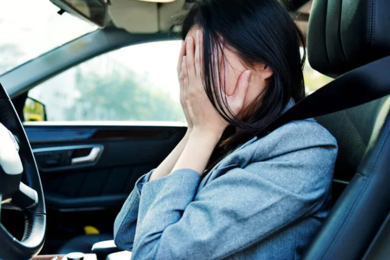 Driver in car covering her face with hands, looking distressed.