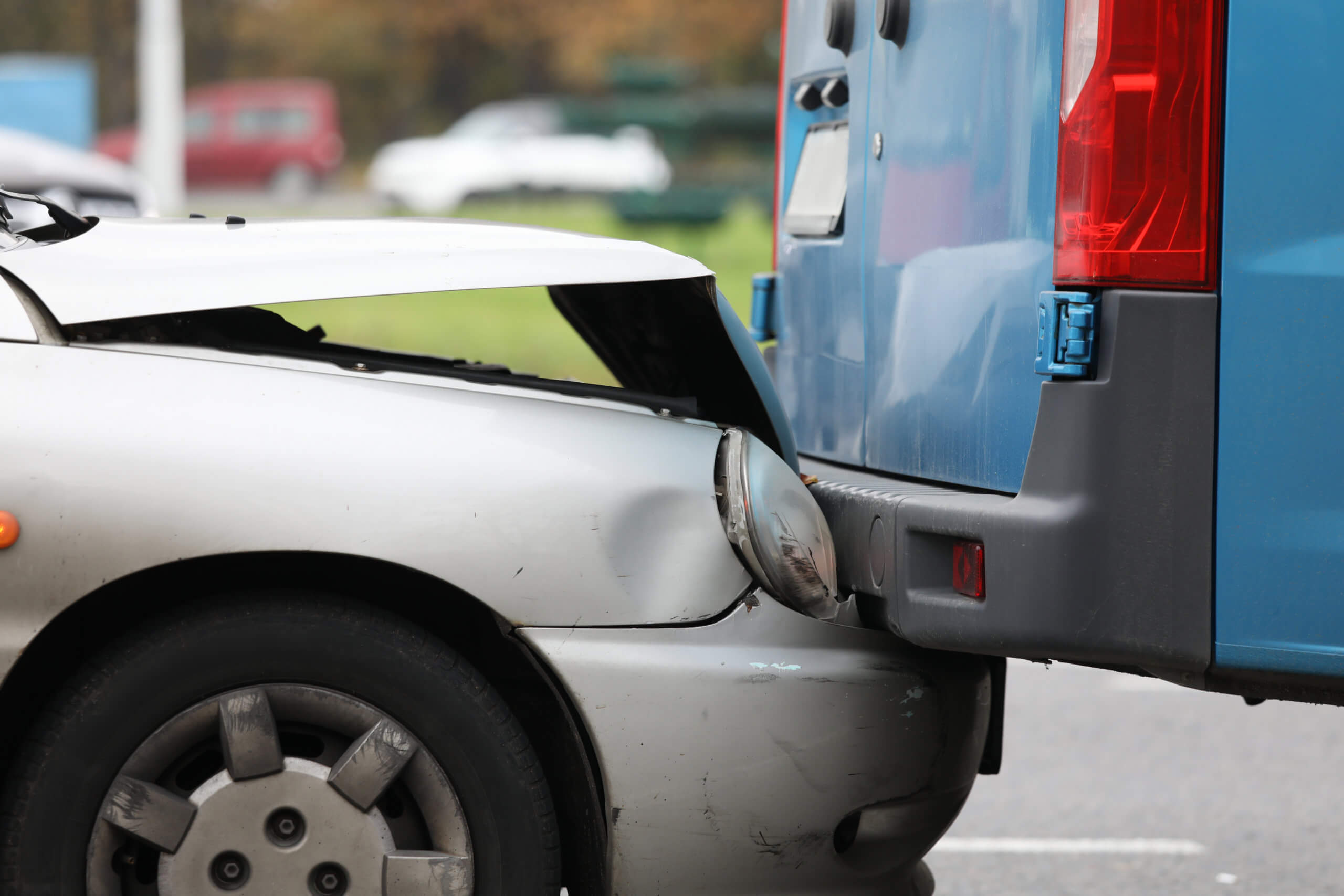 Silver car rear-ends blue van, hood crumpled and headlight damaged.