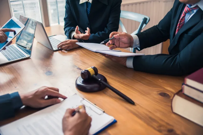 Lawyers meeting at a table with gavel, documents, and laptops.
