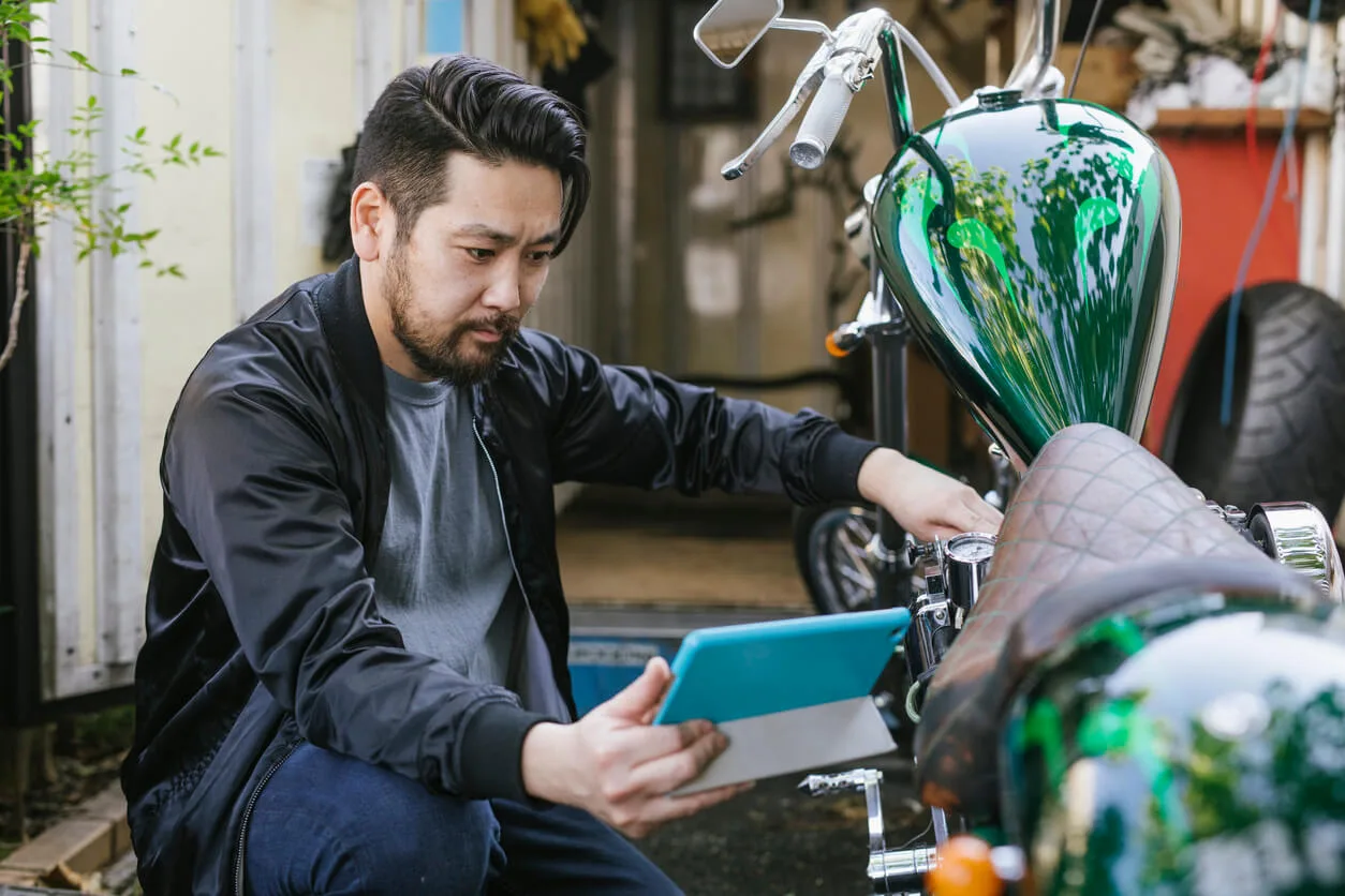 Man using a tablet while inspecting a custom motorcycle in a garage.