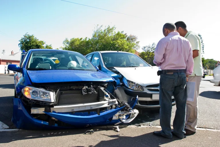 Two men inspect a two-car crash; blue car’s front bumper smashed.