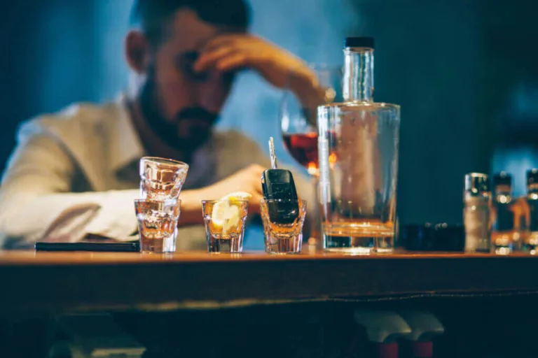 Car keys in a shot glass at a bar with a drinking man.