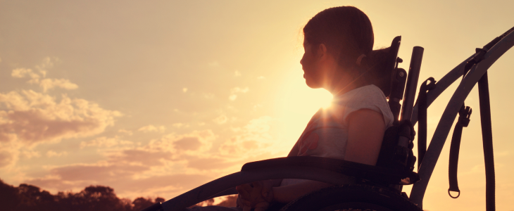 Kid with cerebral palsy in a wheelchair looking at a sunset