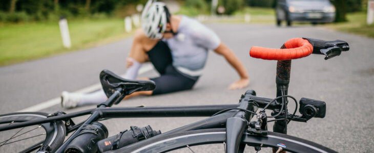 Injured cyclist sitting in pain on the road next to the racing bicycle.